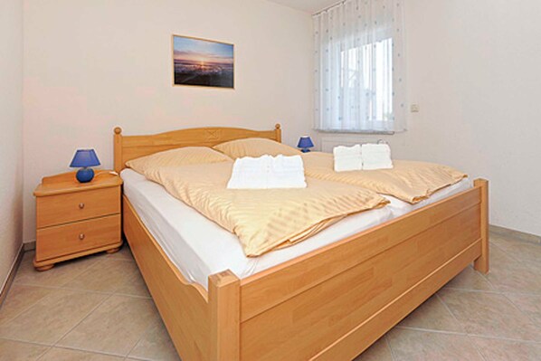 Um quarto individual com cama de madeira, mesa de cabeceira com abajur, janela com cortinas e um quadro na parede.