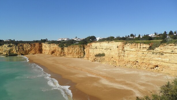 A coastal beach with clear turquoise waters and sandy shores, bordered by cliffs and residential buildings in the background. - Beautiful apartment in a quiet location with sea views  (Porches - Alporchinhos)