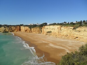 A coastal beach with clear turquoise waters and sandy shores, bordered by cliffs and residential buildings in the background. - Beautiful apartment in a quiet location with sea views  (Porches - Alporchinhos)