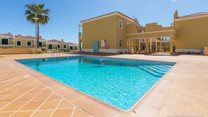 A swimming pool with a geometric tile pattern, surrounded by a patio area with lounge chairs and a palm tree. - Beautiful apartment in a quiet location with sea views  (Porches - Alporchinhos)