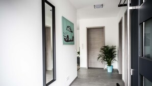 Un couloir moderne avec un grand miroir, un tableau représentant une voiture verte, une plante en pot et une porte donnant sur une autre pièce.