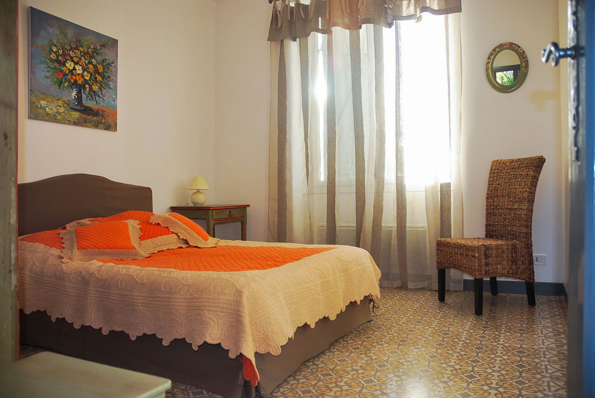Une chambre à coucher comprenant un lit, une chaise, une table de chevet, une lampe, un tableau et une fenêtre avec des rideaux.