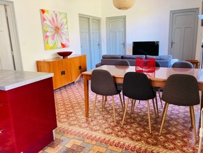A dining area with a wooden table, four chairs, a red cabinet, and a colorful flower painting on the wall.