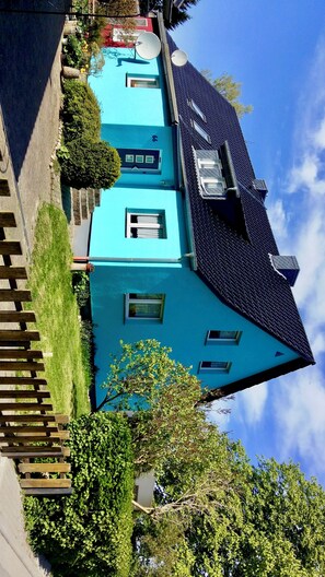 Ein zweistöckiges Haus mit dunklem Dach, blauer Fassade und kleinem Vorgarten mit Holzzaun.