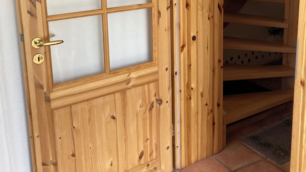 A wooden door with a frosted glass panel and a life preserver emblem, leading to a staircase with wooden steps and a tiled floor.