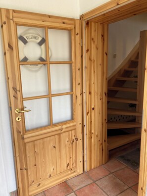 Una porta in legno con un pannello di vetro acidato e un emblema di galleggiante, che dà accesso a una scala con gradini in legno e pavimento piastrellato.