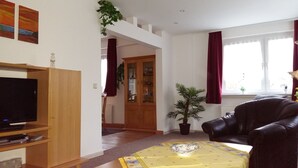 A living room with a TV, a leather sofa, a dining table with a placemat, a potted plant, and a wooden cabinet.
