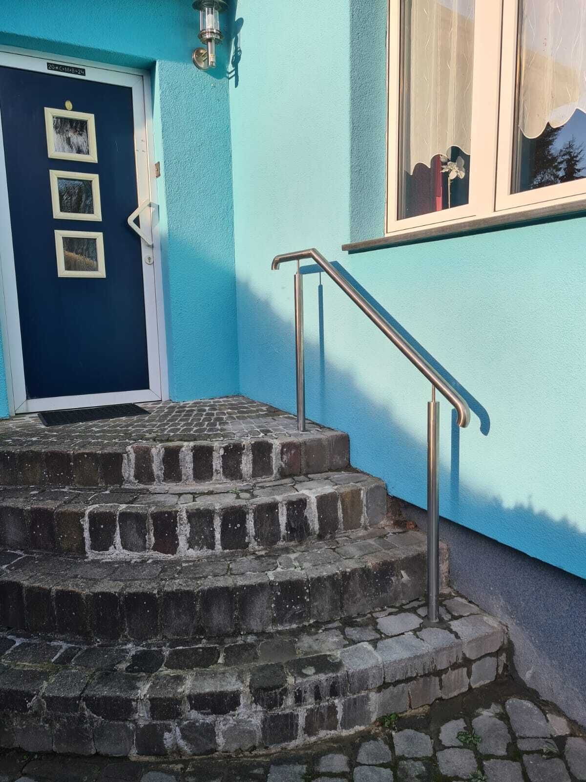 A set of stone steps leading to a door with three framed pictures, a metal handrail, and a window with a curtain.