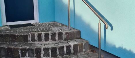 A set of stone steps leading to a door with three framed pictures, a metal handrail, and a window with a curtain.