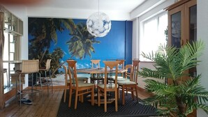 A dining area with a mural of a beach scene, wooden chairs, a round table, and a hanging light fixture.