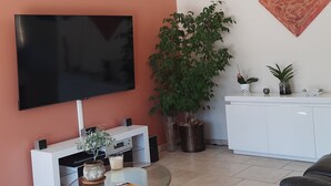 A living room with a flat-screen TV, a glass coffee table, a potted plant, a white cabinet, and a sofa.