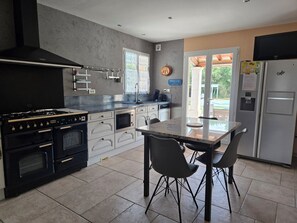 A modern kitchen with a gas stove, oven, microwave, and a built-in dishwasher. There is a dining table with chairs and a large window providing natural light. - BONNIEUX: 4-star house on a wooded lot of 5,500 m. (Bonnieux)