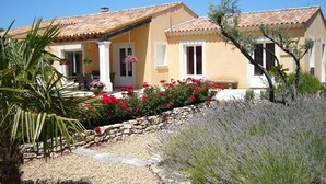 A Mediterranean-style house with a tiled roof, a stone pathway, and a variety of plants including red flowers and lavender.