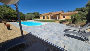 A swimming pool with lounge chairs, a patio area with pebbles, and a house with a tiled roof.
