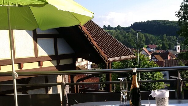 Uma área de refeições ao ar livre com mesa, cadeiras e um guarda-sol verde.