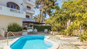 A swimming pool with a stone deck, surrounded by a white building with balconies and a covered outdoor seating area.