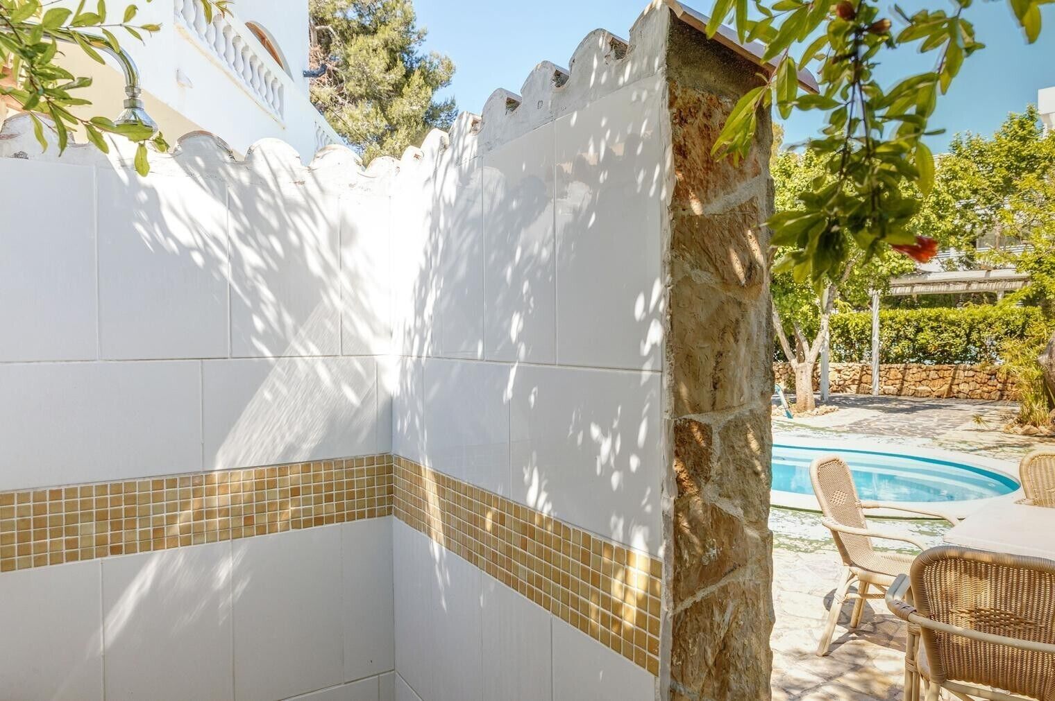A poolside area with a stone wall, tiled flooring, and outdoor furniture.