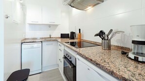 Eine moderne Küche mit weißen Schränken, einer Granit Arbeitsplatte, einem Geschirrspüler, einem Backofen und einer Kaffeemaschine.
