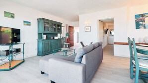 Ein Wohnzimmer mit Sofa, Fernseher, Schrank und Essbereich mit Tisch und Stühlen.