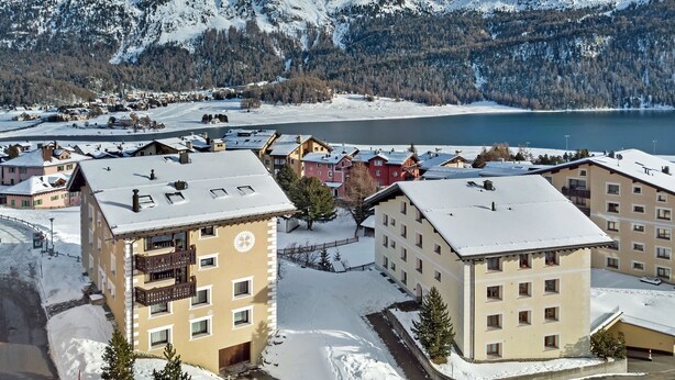 Un paese innevato con edifici, un lago e montagne sullo sfondo.