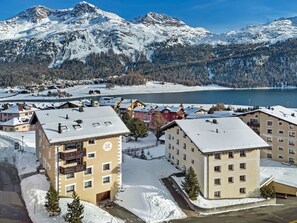 A snow-covered town with buildings, a lake, and mountains in the background. - 4-roomed apartment on the first floor, ca. (Silvaplana)