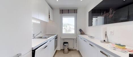 A modern kitchen with white cabinets, a stainless steel sink, a window, and a trash can.