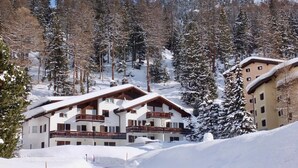 Un refugio de montaña cubierto de nieve con varios balcones y una pista de esquí al fondo.