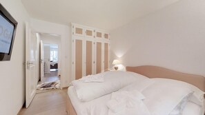 A hotel room with a bed, a nightstand with a lamp, a wardrobe, and a door leading to another room.