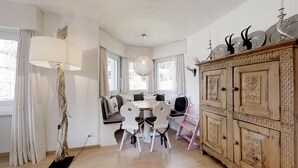 Comedor con una mesa redonda, sillas blancas, una araña y un aparador de madera con adornos.
