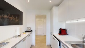 Una cocina estrecha con armarios blancos, una cafetera y un cuadro de ciervos en la pared.