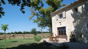 A stone building with a patio area, a table and chairs, and a tree providing shade. - Le Mazet Jean. Camargue Bed and Breakfast (kindling) (Le Cailar)