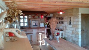 A rustic kitchen with stone walls, wooden ceiling, and a wooden bar area with a vase of dried leaves. - Le Mazet Jean. Camargue Bed and Breakfast (kindling) (Le Cailar)