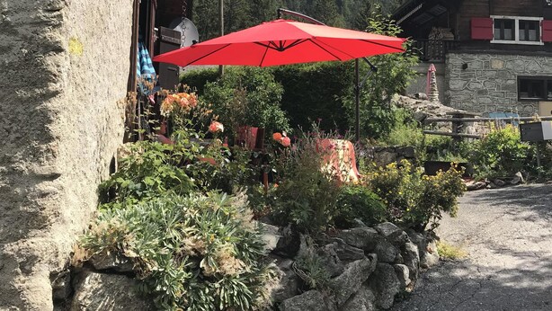 Un edificio rústico con fachada de piedra, un paraguas rojo y un jardín con diversas plantas y flores.