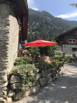 A rustic building with a stone facade, a red umbrella, and a garden with various plants and flowers. - Chalet "Le Grandzon" **** comfortable, quiet (fully renovated chalet) (champex)