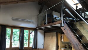 Una mesa de comedor de madera con sillas, un banco, una zona de cocina con armarios y una escalera con barandilla de vidrio.