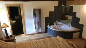 Un dormitorio con cama, mesita de noche, lámpara, baño con bañera, espejo y toallero.