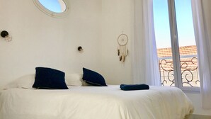 Un dormitorio con cama, dos almohadas, un atrapasueños, un espejo redondo y una ventana con vista a un edificio.