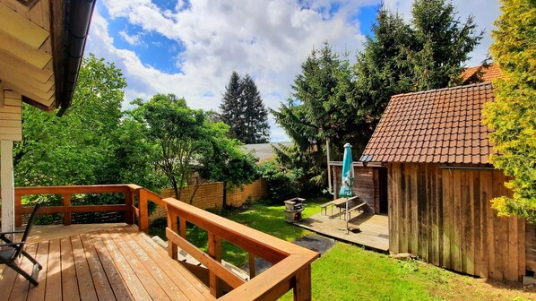 A wooden deck with a bench, a small shed, and a grassy yard with trees. - Cozy evenings in the log cabin, by the fireplace and in the wood-fired Finnish sauna (Schefflenz)