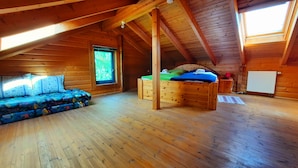 A cozy attic bedroom with a wooden floor, a bed, a sofa, and a window with a view.