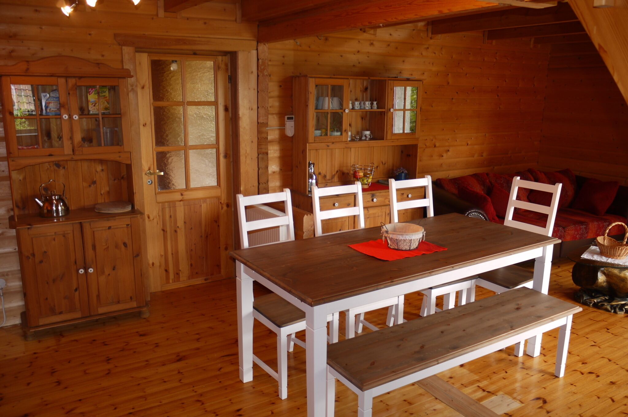 Un interno in legno con un tavolo da pranzo, sedie bianche, una panca e mobili contenitori in legno.