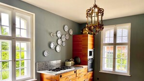 A kitchen with a granite countertop, wooden cabinets, a microwave, and a gas stove. There are several decorative plates on the wall and a chandelier. - Small castle Lanke (Lanke)