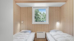 Une petite chambre accueillante avec deux lits, une fenêtre donnant sur les arbres et un plafond blanc.