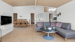 Un salon moderne avec un téléviseur, une table à manger en bois et un canapé gris agrémenté d’une table basse en verre.