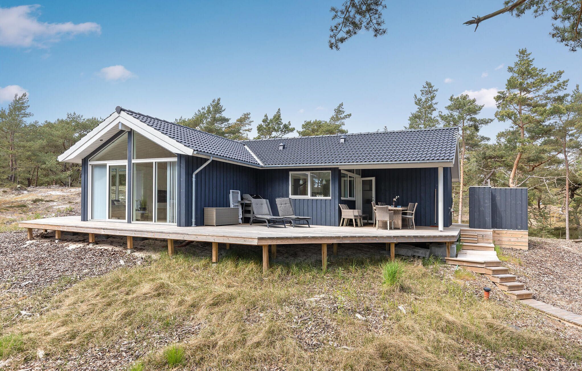 A modern house with a large deck, a covered outdoor seating area, and a view of the surrounding forest.