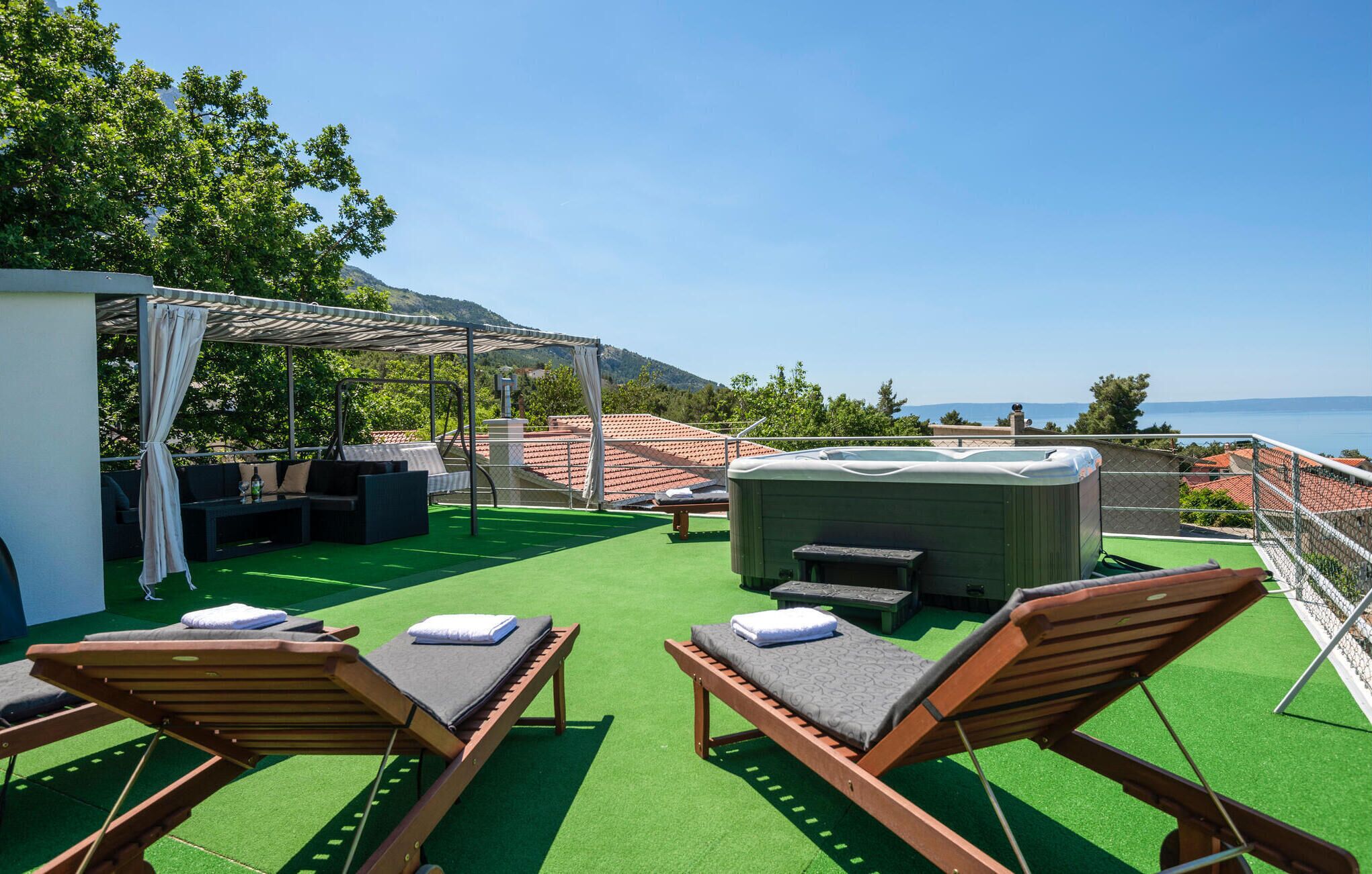 En takterrass med solstolar, ett bubbelbad och en pergola.