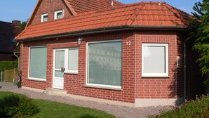 Een rood bakstenen huis met een schuin dak, grote ramen en het cijfer '12' op de zijkant.
