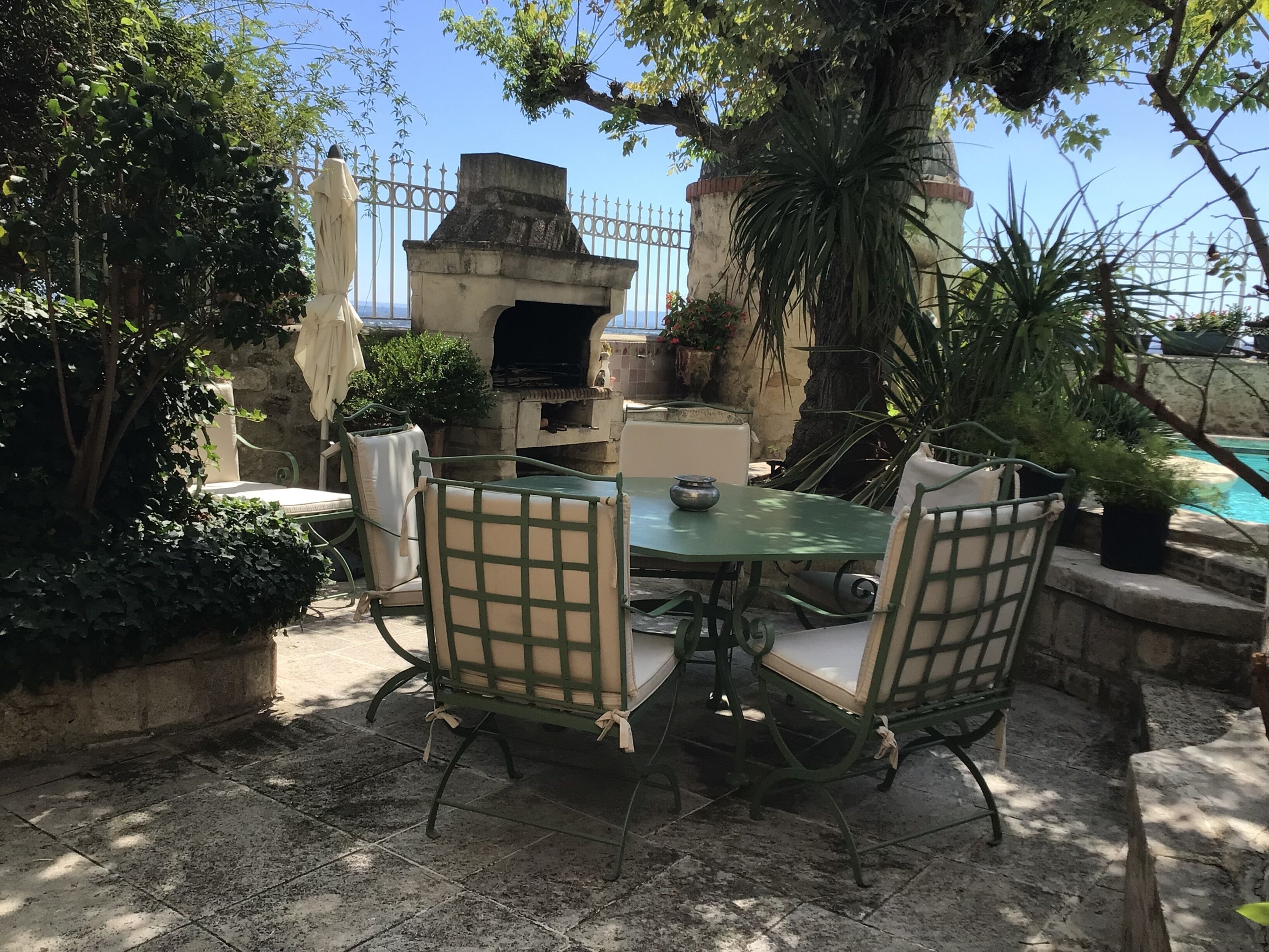 Un patio al aire libre con una mesa redonda y cuatro sillas, un horno de piedra y una piscina al fondo.