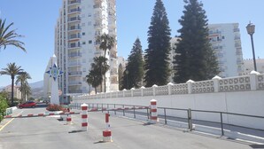 Un edificio residencial de varios pisos con balcones, una cerca decorativa y palmeras.