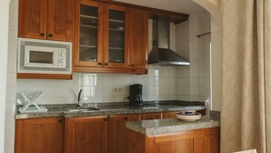 Una cocina con armarios de madera, microondas, cafetera y lavamanos.
