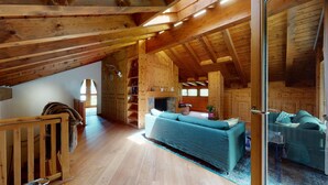 A spacious loft with wooden beams, a large sofa, and a fireplace.